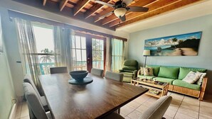 A dining area with a wooden table, chairs, and a bowl. There is a green sofa and a painting of a beach scene on the wall. - A6 Modern 3BR with Stunning Views! (San Pedro)