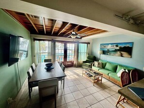 A dining area with a table and chairs, a sofa, a television mounted on the wall, and a ceiling fan.
