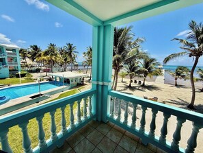 A balcony with a view of a pool, beach, and palm trees. - B2 Tropical 3BR Stunning Reef Views (San Pedro)