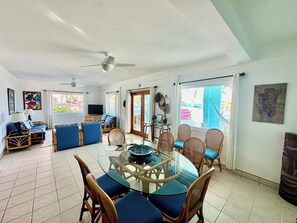 Un amplio salón con mesa de vidrio, mobiliario de mimbre y ventilador de techo.