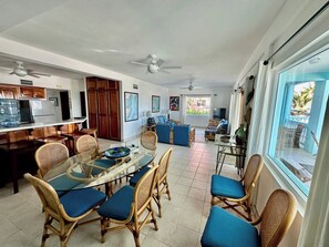 Amplia sala de estar con mesa de comedor, sillas, sofá y vista a través de un ventanal.