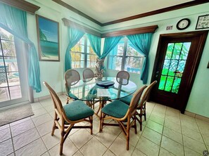 A dining area with a glass table, wicker chairs, teal curtains, and a view through a window.