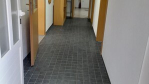 Un pasillo estrecho con suelo de baldosas grises oscuras y puertas de madera.
