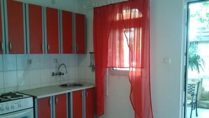 A compact kitchen with red cabinets, a white countertop, a sink, and a window with red curtains. - Apartments Marija in National Park Area - One Bedroom Apartment in Ground Floor (Starigrad-Paklenica)