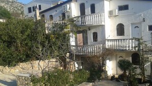 A multi-story building with balconies, a stone pathway, and surrounding vegetation. - Apartments Marija in National Park Area - One Bedroom Apartment in Ground Floor (Starigrad-Paklenica)
