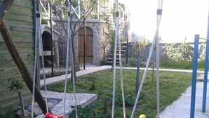 Two swings in a backyard with a stone wall and a wooden house in the background. - Apartments Marija in National Park Area - One Bedroom Apartment in Ground Floor (Starigrad-Paklenica)