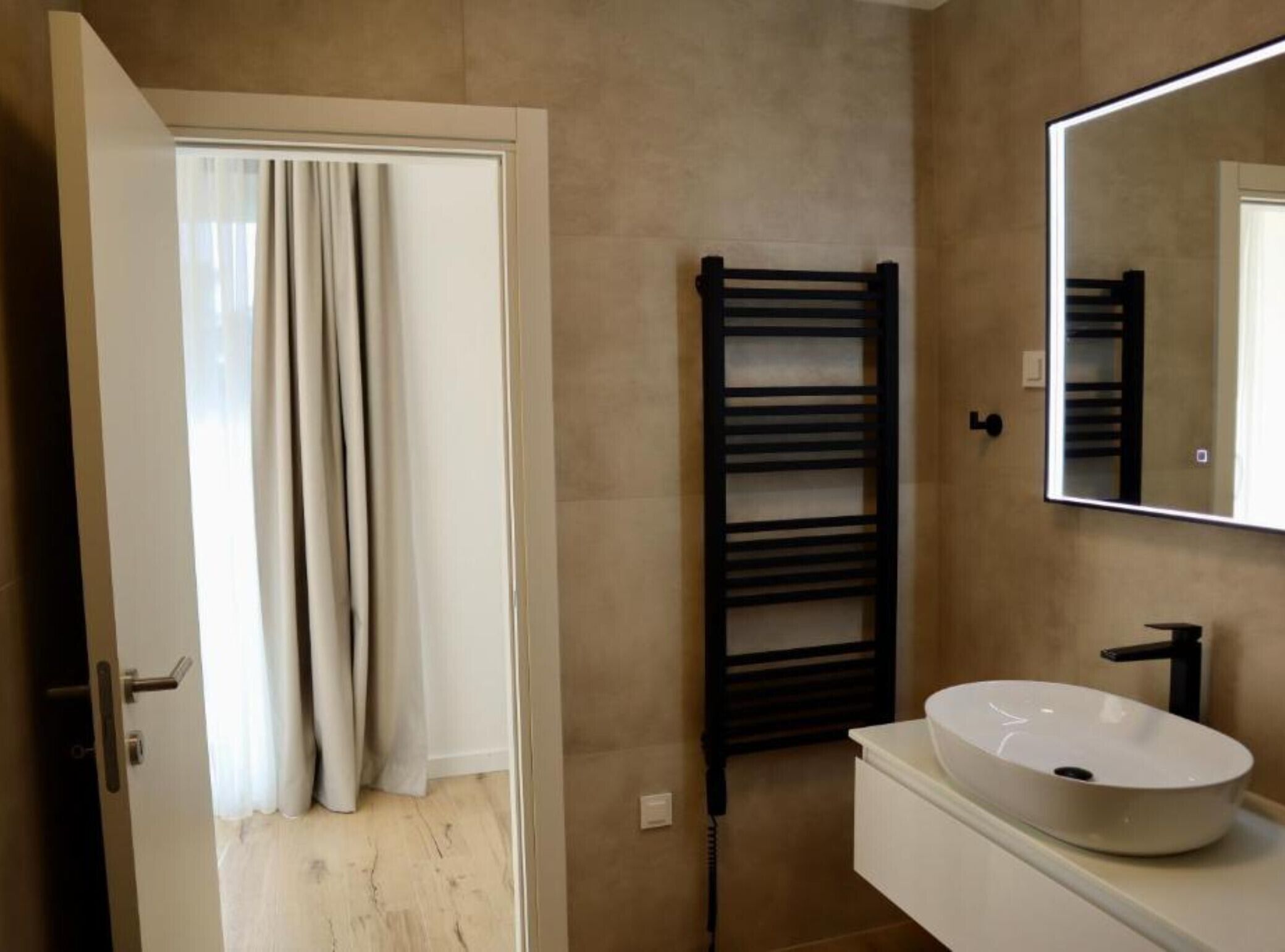 Un baño con un lavamanos blanco, un espejo y un perchero para toallas.