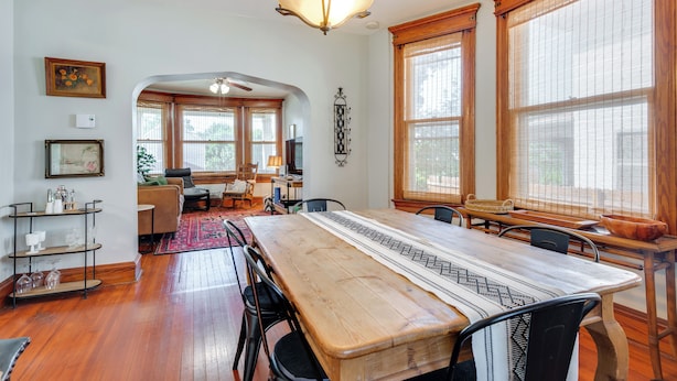 A spacious dining area with a long wooden table, surrounded by chairs, and large windows with wooden frames.