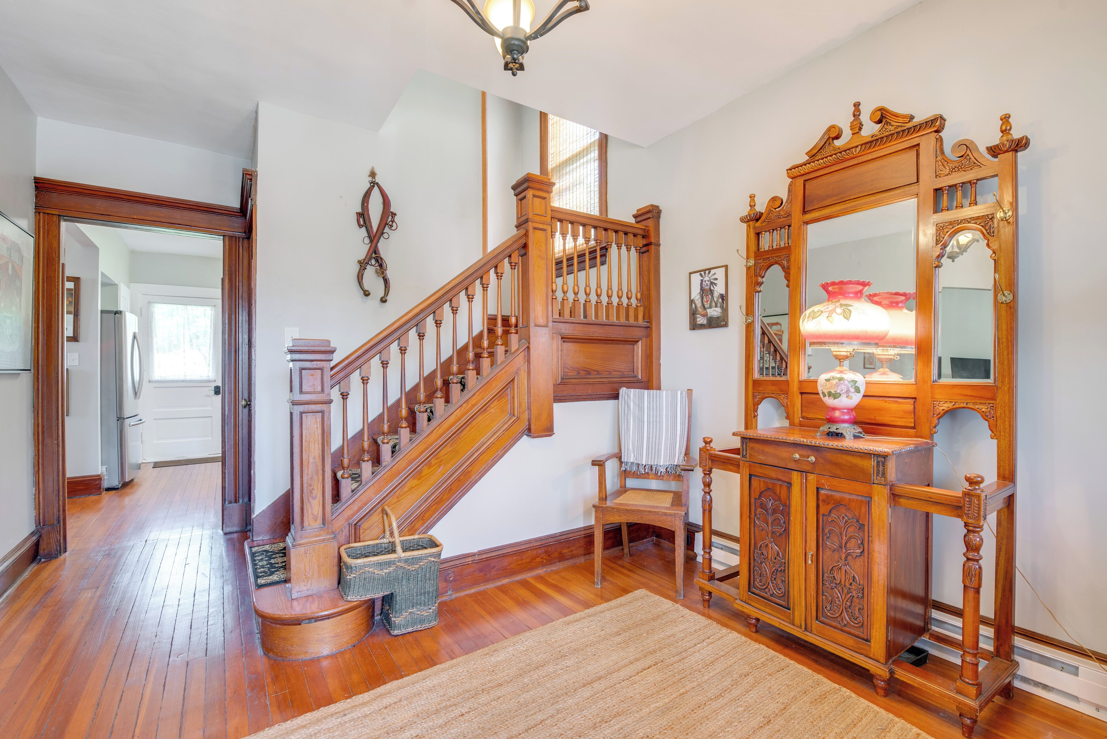 Un escalier en bois avec une rampe, un meuble en bois avec un miroir et une chaise avec une serviette.