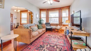 A living room with a sofa, a coffee table, a TV, and a large window with blinds.