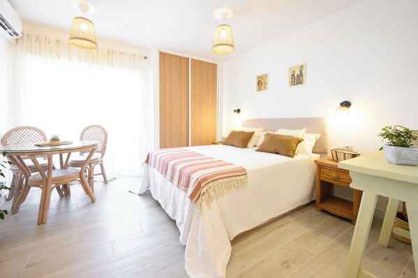 Ein Schlafzimmer mit Bett, Nachttisch, Lampe und einem Essbereich mit Stühlen und Tisch.