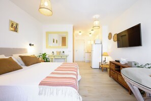 Ein Hotelzimmer mit Bett, Nachttisch, Lampe, Fernseher und Blick auf Küche und Bad.