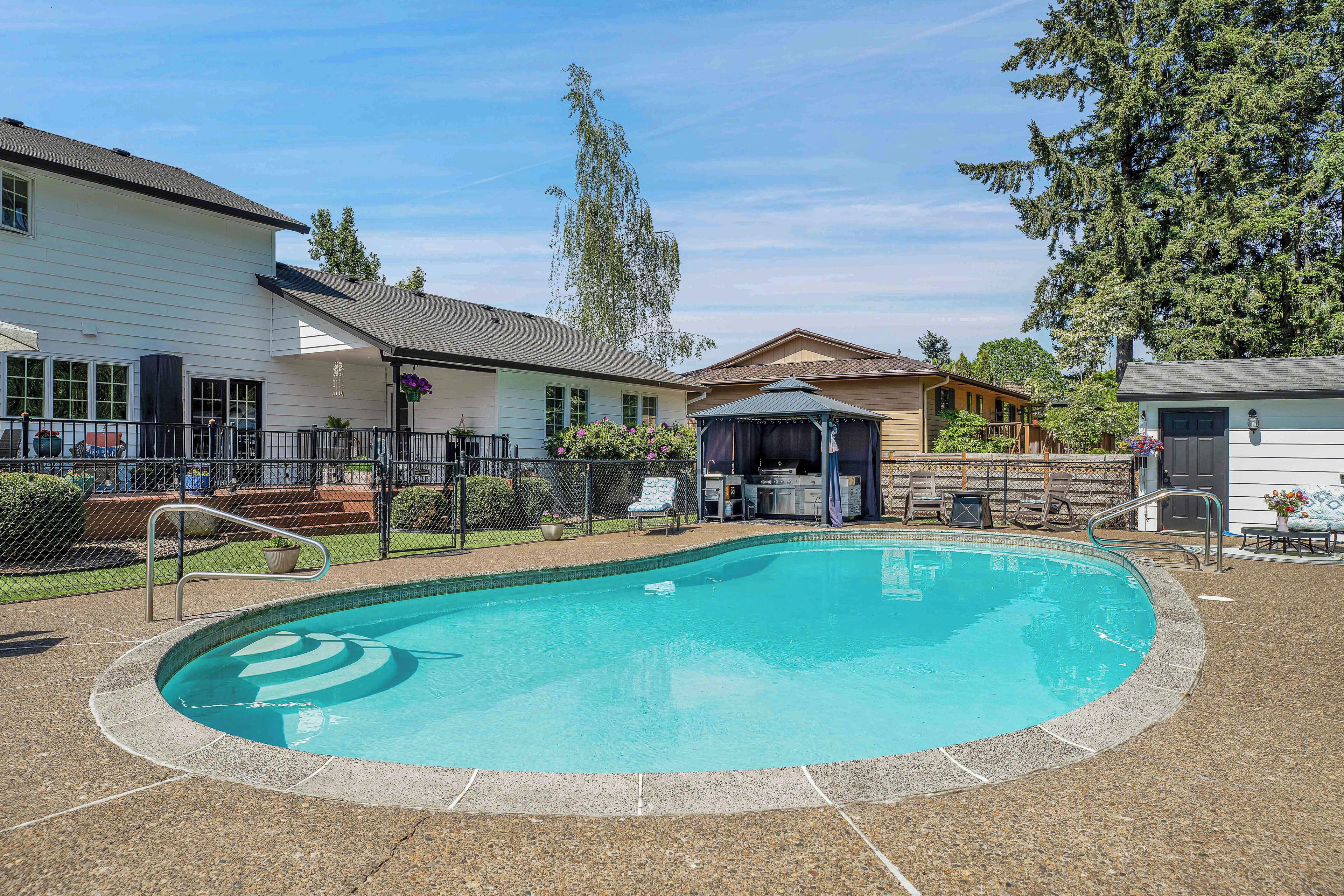 A swimming pool with a gazebo, a fenced patio area, and a building with a porch.