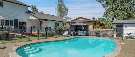 A swimming pool with a gazebo, a fenced patio area, and a building with a porch.