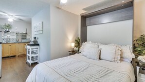 Un dormitorio con una cama grande, una mesita de noche, un ventilador de techo y vistas a la cocina.