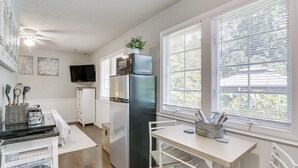 Una cocina compacta equipada con refrigerador, microondas y estufa, una mesa de comedor y una ventana con persianas.