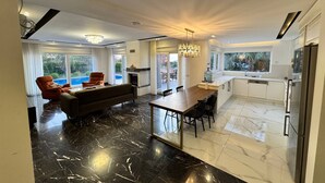 A modern living room with a fireplace, a dining area with a marble floor, and a kitchen with white cabinets and a refrigerator. - Entire villa in Keşefli, Turkey (Keşefli)