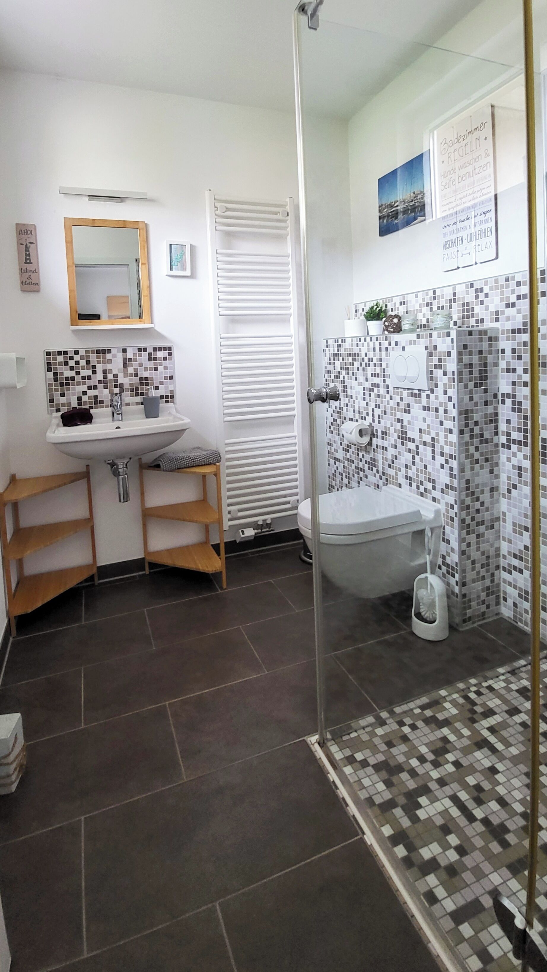 Ein Badezimmer mit Waschbecken, Spiegel und Toilette. Es gibt eine Duschkabine mit Glastür und Fliesenboden.