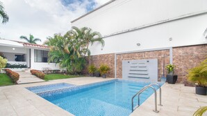 A swimming pool with a tiled deck, surrounded by potted plants and a building with a tiled roof. - Casa Blau (Cali)