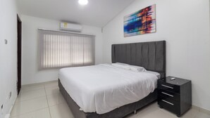 A bedroom with a bed, a nightstand, a wall-mounted air conditioner, a window with blinds, and a colorful abstract painting. - Casa Blau (Cali)