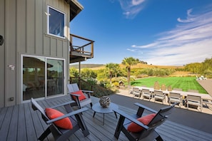 A deck with outdoor furniture and a view of a well-maintained lawn and hills.