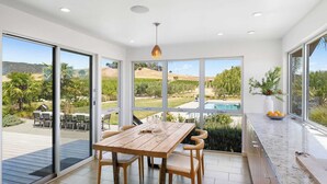 A spacious room with a wooden dining table, large sliding glass doors, and a view of a swimming pool and hills.