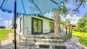 Eine Terrasse mit Tisch und Stühlen, ein überdachter Bereich mit einem Baum und ein Gebäude mit großen Fenstern.