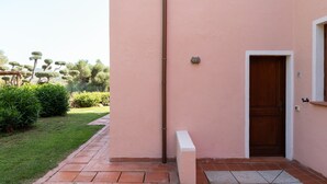 A pink building with a wooden door, a small white bench, and a tiled pathway leading to the entrance. - Terrazza al Poggio Vista Mare by Wonderful Italy (Porto Rotondo)