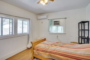 Ein Schlafzimmer mit einem hölzernen Bett, einer Klimaanlage, einem Fenster mit Vorhängen und einem Deckenventilator.