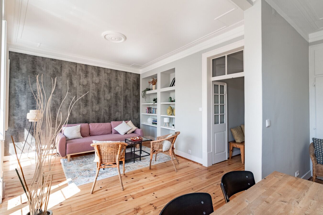 Ein stilvolles Wohnzimmer mit einer Couch, Korbstühlen, einem Couchtisch und einem Bücherregal.