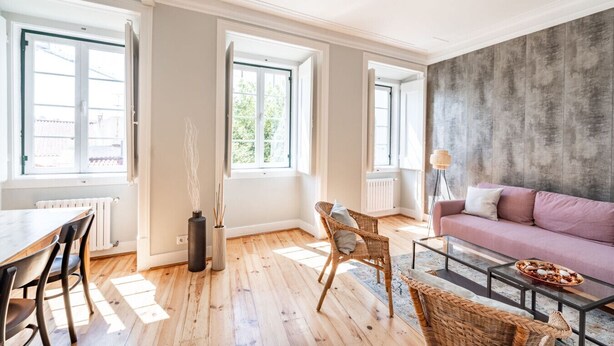 Un salon spacieux doté d’un plancher en bois, d’un canapé rose, de fauteuils en osier, d’une table à manger avec des chaises et de grandes fenêtres laissant entrer la lumière naturelle.