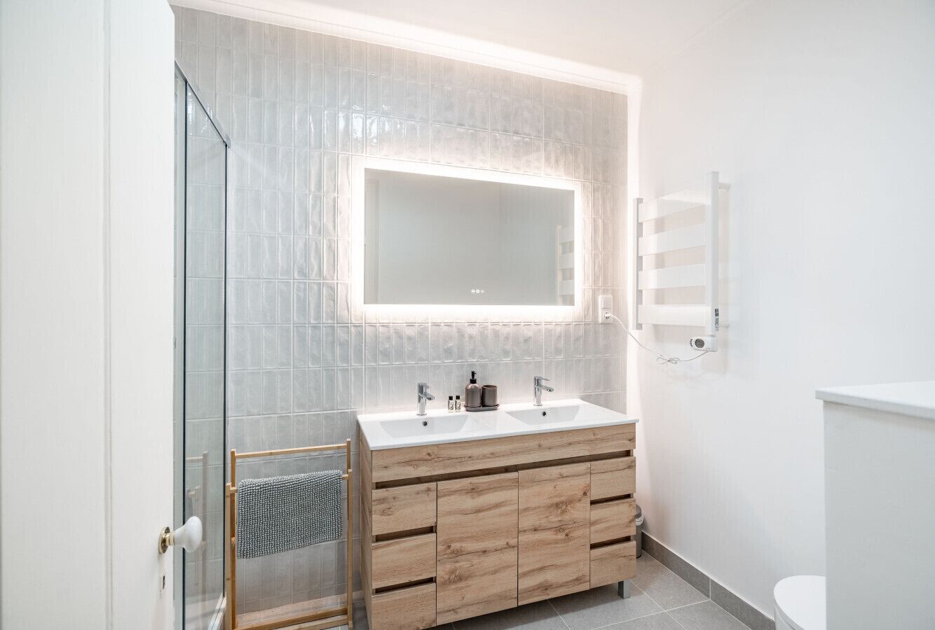 A modern bathroom with a glass shower enclosure, a double sink vanity with wooden cabinets, and a large mirror above the sink.