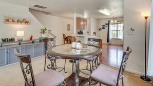 Een eetgedeelte met een ronde glazen tafel, vier stoelen en een keuken op de achtergrond.