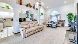 A spacious living room with a beige leather sofa, a coffee table, and a fireplace. There is a kitchen area with white cabinets and a dining table. - Pool & Dock! Canal-Front Port Charlotte Home (Port Charlotte)