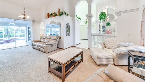 A spacious living room with a beige leather sofa, a striped sofa, and a coffee table. There are large windows with arched frames and a view of the outdoors. - Pool & Dock! Canal-Front Port Charlotte Home (Port Charlotte)
