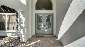 A house entrance with a white exterior, a tiled porch, and a double door with glass panels. - Pool & Dock! Canal-Front Port Charlotte Home (Port Charlotte)