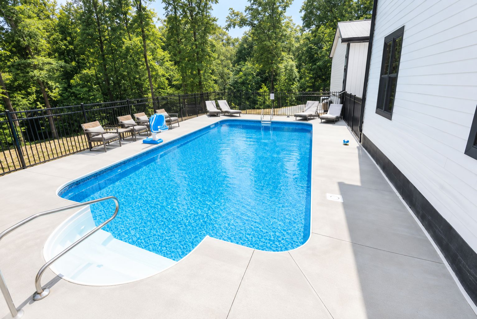 A rectangular swimming pool with a ladder, surrounded by lounge chairs and a fence.