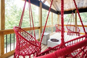 A wooden deck with red macramé chairs and a small table with a fire pit.