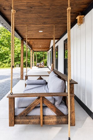 A covered outdoor seating area with wooden swing seats and a view of a building with large windows.