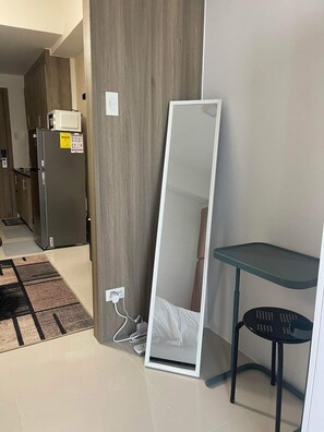 A room with a wooden wall, a white-framed mirror leaning against it, a black chair, and a small table. - Fame Residences Mandaluyong by darpm (Mandaluyong)