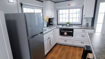 A modern kitchen with a stainless steel refrigerator, white cabinets, a built-in oven, and a wooden floor.