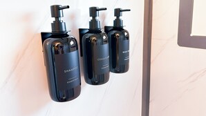 Three black bottles of body wash and shampoo with pumps, labeled 'Essentials', mounted on a white marble wall. - Iron Horse Living - 1 Bed Studio (Odessa)
