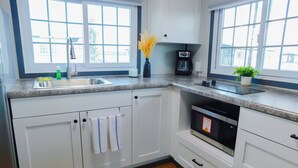 A modern kitchen with white cabinets, a granite countertop, a built-in dishwasher, and a window with a view of the outside. - Iron Horse Living - 1 Bed Studio (Odessa)