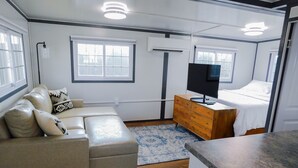 A compact, well-lit room with a sofa, a wooden dresser, a bed, and a television. - Iron Horse Living - 1 Bed Studio (Odessa)
