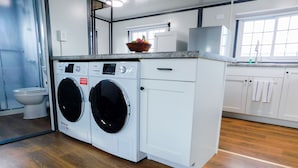 A compact, modern laundry room with two front-loading washing machines, a stainless steel range hood, and a wooden floor.