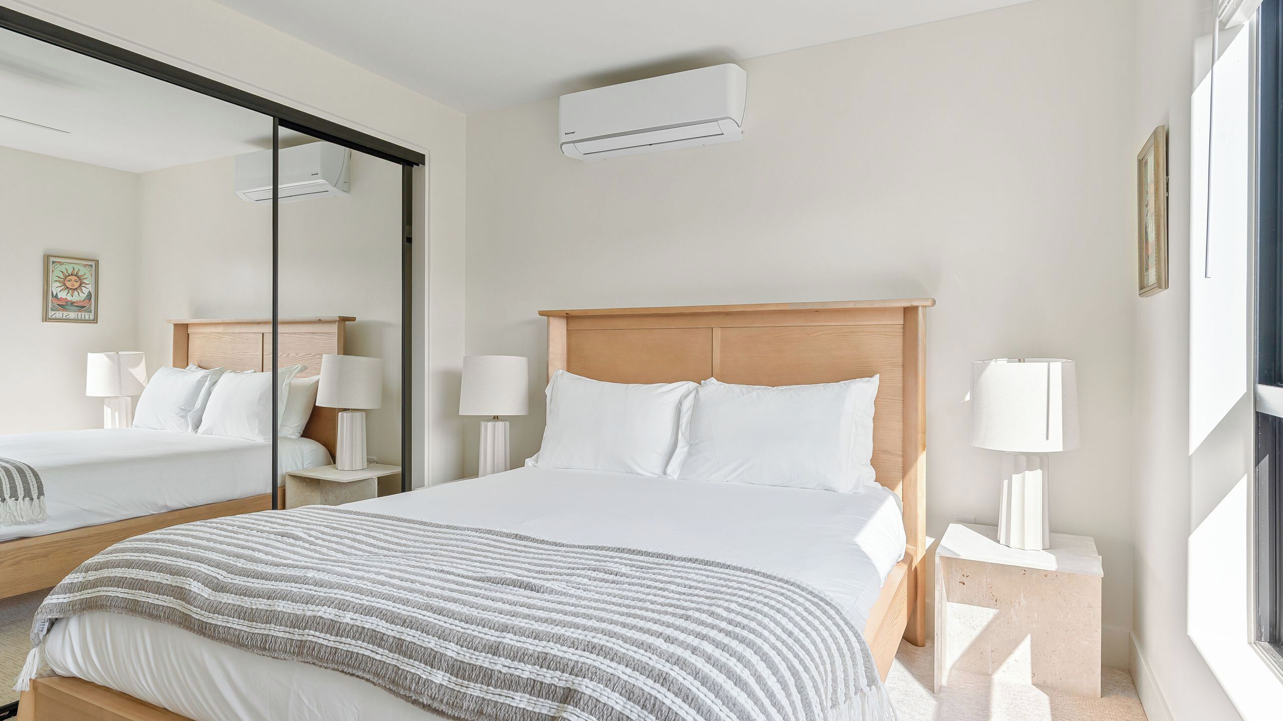 Une chambre d’hôtel avec un grand lit, des lampes de chevet, une tête de lit en bois, un miroir et un appareil de climatisation.