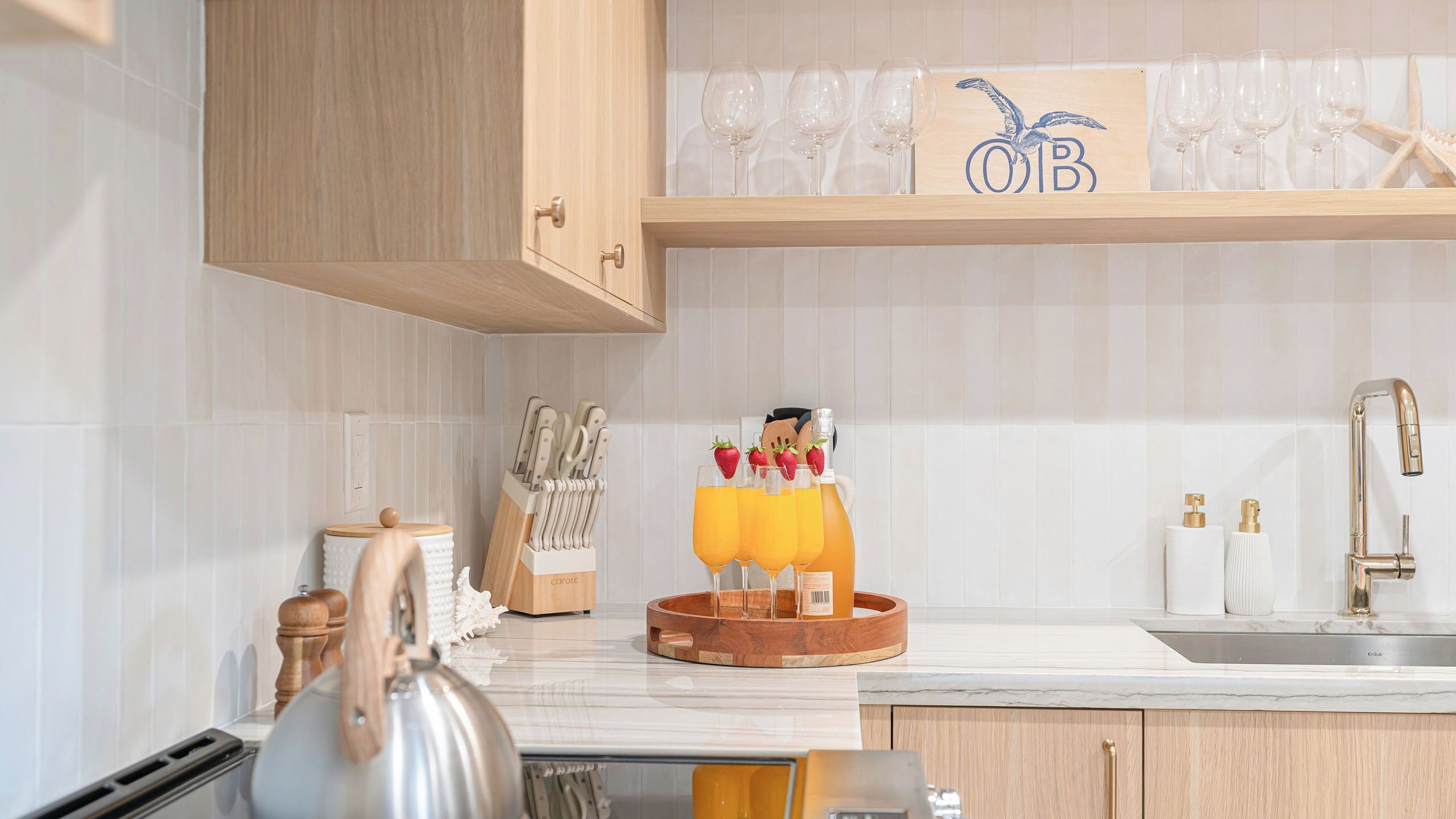A kitchen with wooden cabinets, a countertop with a kettle, a fruit bowl, and a wine rack.