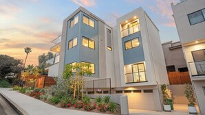 A modern multi-story residential building with a flat roof, large windows, and a well-maintained garden with various plants and flowers. - Modern 5bdr, Mins to Sunset Cliffs & Ocean Beach Point View Luxe by Avantstay (San Diego)