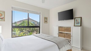 A bedroom with a bed, a TV, a window with a view of a house and greenery, and a wall with two framed pictures. - Modern 5bdr, Mins to Sunset Cliffs & Ocean Beach Point View Luxe by Avantstay (San Diego)