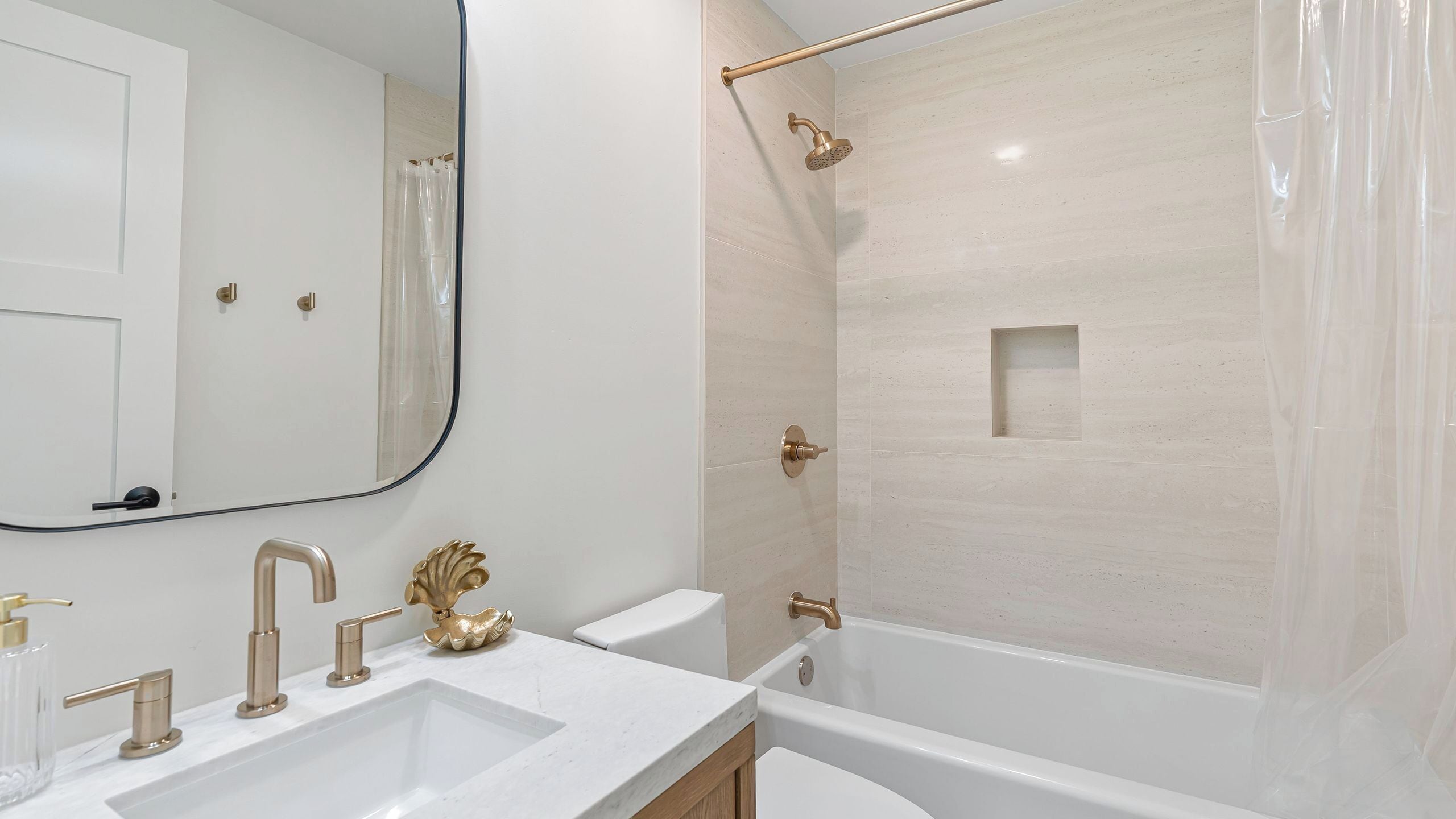 A modern bathroom with a large mirror, a bathtub, a shower with a glass door, and a vanity with a gold faucet.